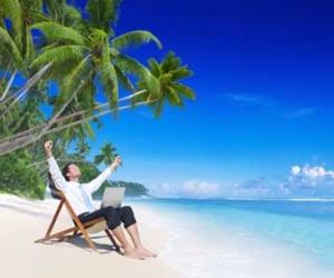 Digital nomad is working on laptop at tropical beach with arms raised