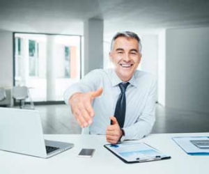 Smiling recruiter reaches across desk to shake hands with job candidate