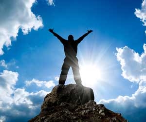 Silhouette of successfl man on top of mountain with clouds and blue sky