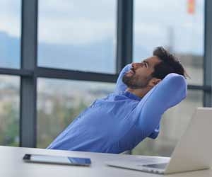 Happy employee sits back at office and enjoys work