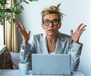 Shocked woman with wide eyes and hands up in front of her computer