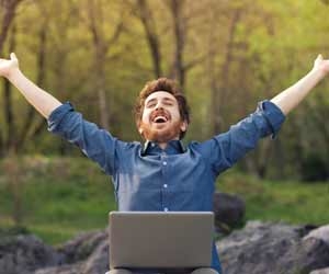 Man working outdoors on laptop with arms in air