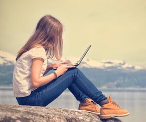 Freelance writer working on laptop on rock next to mountain lake