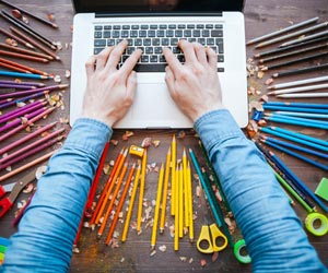 Hands working on laptop with a variety of colored pencils