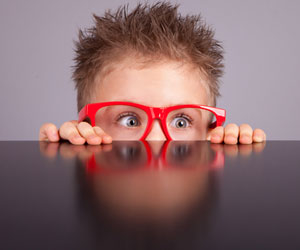 Scared child in glasses peeks over a table