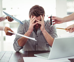 A stressed out worker covering his face when asked to do too many things