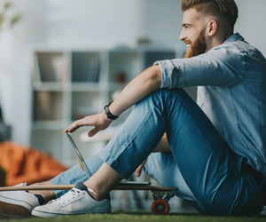 Man sitting with a laptop on top of a skateboard