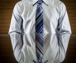 Body of a man in shirt and tie sitting at desk with a mirror image in the desk's reflection