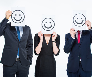 Three business professionals holding sheets of paper with smiley faces printed on them